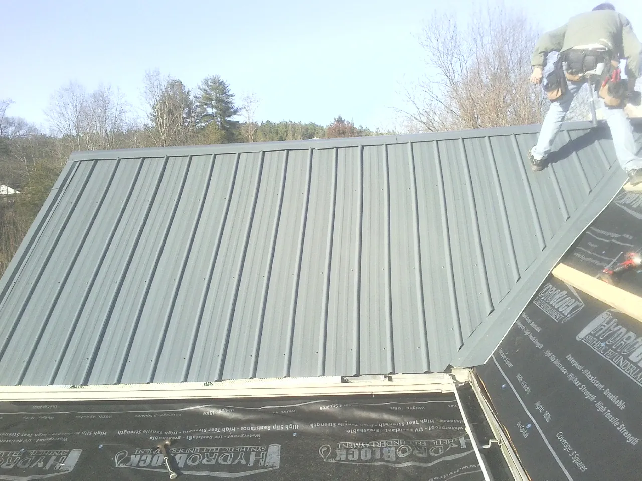 Crew installing dark green standing seam panels over synthetic underlayment in Arlington
