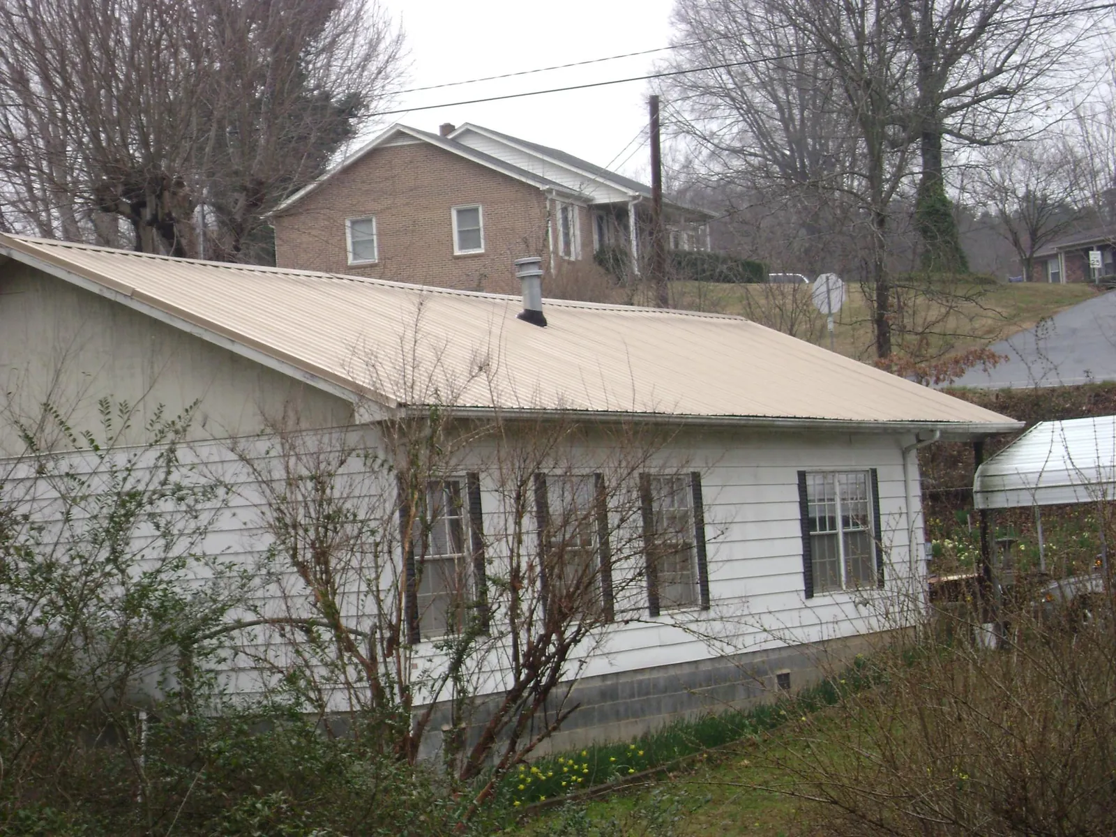 Tan metal roof on a white sided house set into a hillside — Commercial Roofing by Roofing Brothers in Arlington
